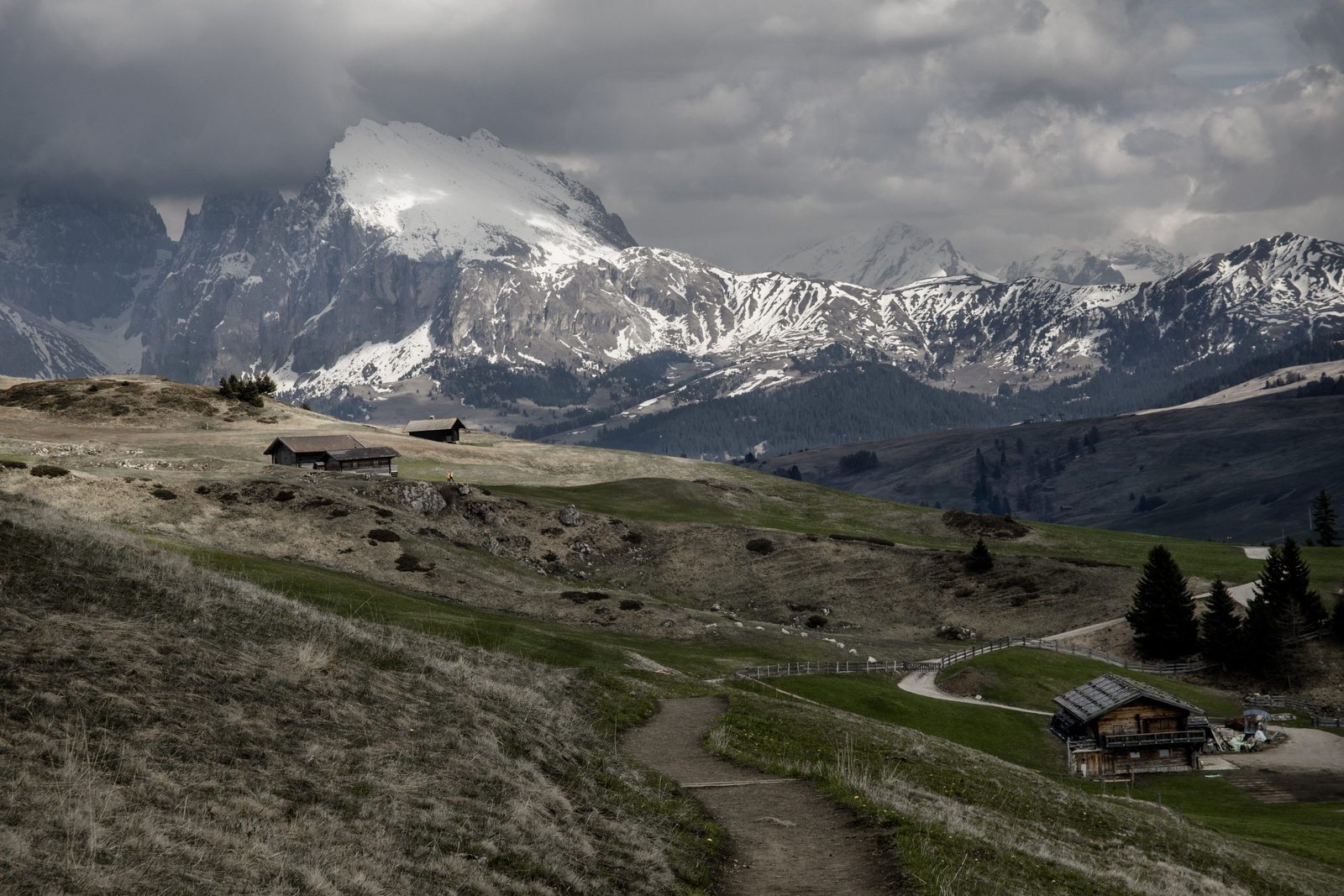 A wide shot of a small cabins near mountains covered with snow under a cloudy sky